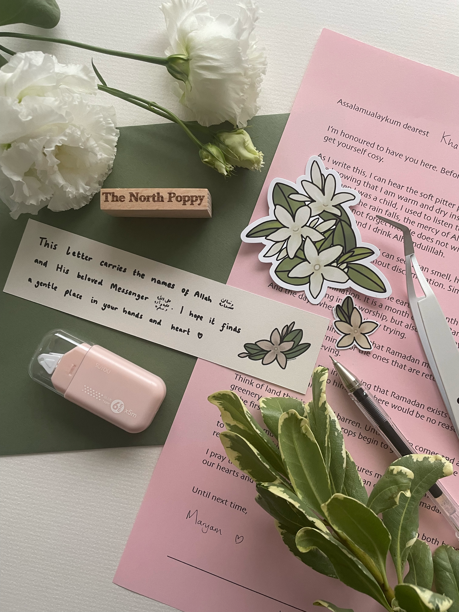 Stationery items including flowers, a rubber stamp, and a pen on a pink surface.