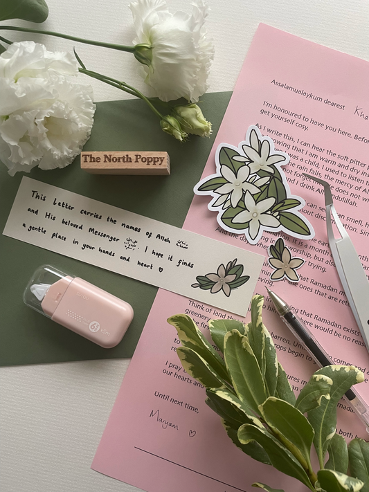 Stationery items including flowers, a rubber stamp, and a pen on a pink surface.